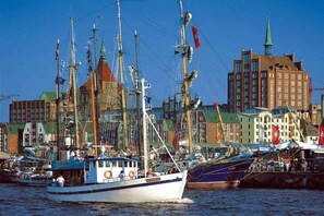 Ein Hafen mit mehreren angestaubten Booten, ein markantes Gebäude mit einem grünen Turm und verschiedene weitere Bauten im Hintergrund.