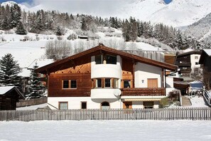 A two-story chalet with a wooden facade, a balcony, and a view of a snowy mountain landscape. - Holiday apartment with 1 bedroom (Pettneu am Arlberg)