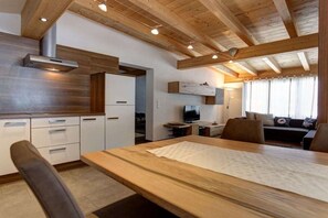 A modern kitchen with wooden beams, a dining area with a table, and a living space with a sofa. - Holiday apartment with 1 bedroom (Pettneu am Arlberg)