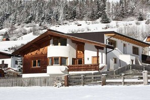 Un chalet de dos pisos con fachada de madera, un balcón y una escalera que conduce al piso superior.
