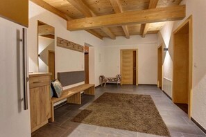 Un pasillo amplio con vigas de madera, un banco, una alfombra y una puerta.