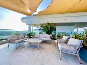 A modern outdoor seating area with sofas and a coffee table, surrounded by potted plants and overlooking a cityscape. - Luxury studio with amazing rooftop pool near the beach (Mombasa)
