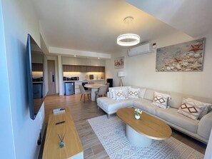 A modern living room with a sofa, coffee table, and a TV mounted on the wall. - Luxury studio with amazing rooftop pool near the beach (Mombasa)