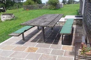 A patio with a wooden table and benches, surrounded by stone tiles. - Holiday home with 4 bedrooms (Riefensberg)