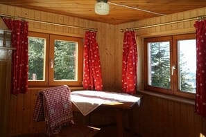 A cabin room with wooden walls, a bed with a checkered blanket, and two windows with red curtains. - Holiday home with 4 bedrooms (Riefensberg)