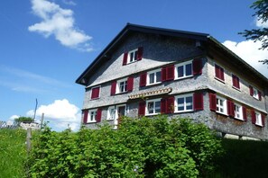 A multi-story building with red shutters, a stone facade, and a clear sky. - Holiday home with 4 bedrooms (Riefensberg)