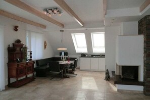 A spacious living area with a fireplace, a dining table, and a kitchen in the background. - Holiday apartment with 2 bedrooms (Stainz)