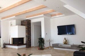 Una sala de estar moderna con chimenea, un televisor de pantalla plana montado en la pared y una escalera que sube a otro nivel.