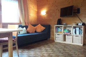 Une pièce comprenant un canapé, un téléviseur fixé au mur, une bibliothèque et une fenêtre avec des rideaux.