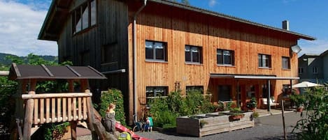 A wooden building with a sloped roof, a covered outdoor area with seating, and a playground.