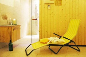 Une pièce avec un mur en bois, une chaise à rayures jaunes, une petite table avec une bougie et un vase contenant des plantes séchées.