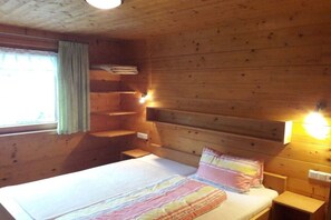 A wooden cabin room with a bed, a window with curtains, and a shelf. - Apart Greber Bersbuch (Andelsbuch)