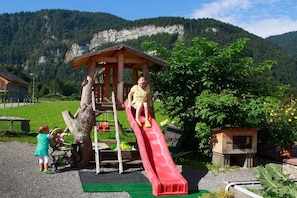 A playground with a slide and climbing structure, surrounded by greenery and mountains. - Apart Greber Bersbuch (Andelsbuch)