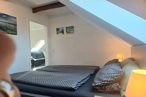 Een slaapkamer met dakraam, een bed met behang, een bedlampje en twee aan de muur hangende afbeeldingen.