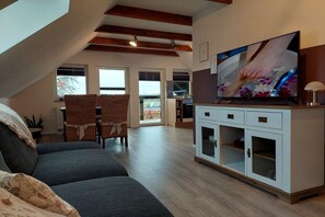 Ein Wohnzimmer mit hoher Decke, einem Fernseher, einer Couch, einem Schrank und Blick durch ein Fenster.