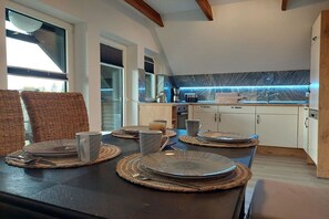 A modern kitchen with a dining area, featuring a dark wooden table, woven chairs, and a kitchen counter with a blue backsplash. - Holiday apartment with 1 bedroom (Blumenholz OT Weisdin)