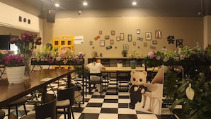 L’intérieur d’un restaurant avec un sol à carreaux, des tables, des chaises et divers éléments de décoration murale, notamment des tableaux encadrés et des panneaux.