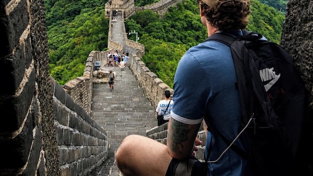 Une personne assise sur un mur de pierre, d’où elle contemple la Grande Muraille de Chine, avec en arrière-plan de luxuriantes montagnes verdoyantes.