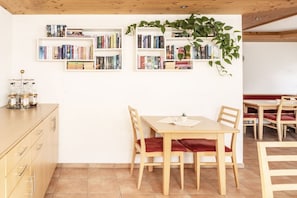 Ein Essbereich mit einem Holztisch und Stühlen, umgeben von Bücherregalen mit Büchern und einer hängenden Pflanze.