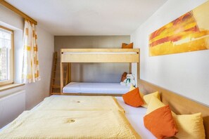 Ein Schlafraum mit Etagenbett, einer Leiter, einem Fenster mit Vorhängen, einem Bett mit Kissen und einem Bild an der Wand.