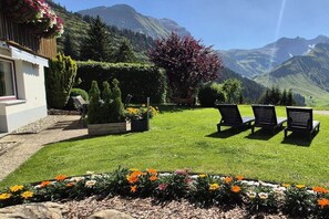 Ein Hotelzimmer mit Bergblick, einem Blumengarten und zwei Liegestühlen.