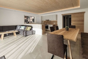 A modern living room with a sofa, a dining table, and a kitchen in the background. - 80m² Guesthouse Sonne (Bichlbach)