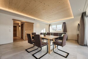 Ein moderner Essbereich mit Holztisch und -stühlen, einer Couch und einem Fenster mit Vorhängen.