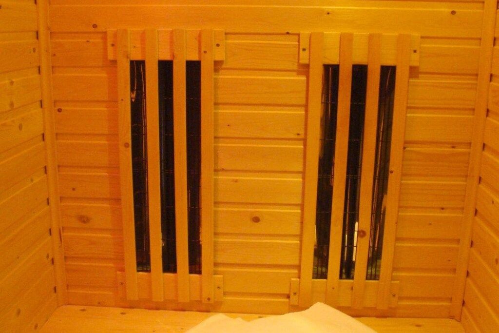 A wooden cabin interior with a single bed and two windows with vertical blinds.