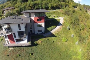 Una casa moderna de dos pisos amb un balcó, envoltada per un turó verd i exuberant.