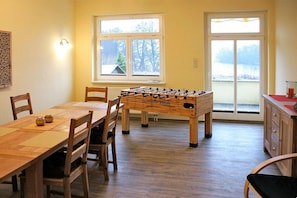 A room with a foosball table, wooden chairs, a dining table, and a view through a window. - Feldberger Hütte Forestry House (Feldberger Seenlandschaft)