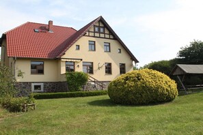 A two-story house with a red-tiled roof, a stone foundation, and a well-maintained lawn with a large bush. - Feldberger Hütte Forestry House (Feldberger Seenlandschaft)