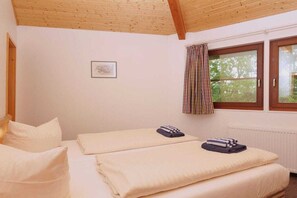 A room with two beds, a window with curtains, a radiator, and a framed picture on the wall. - 2 in the Canadian beach bungalow (Seebad Ahlbeck)