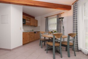 Eine Küche mit Holzschränken, einem Esstisch mit Stühlen und einem fenster mit Vorhängen.
