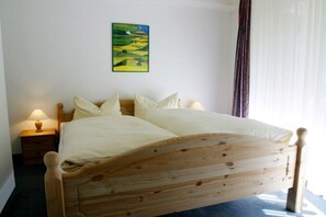 Ein hölzernes Bett mit weißer Bettwäsche, ein Nachttisch mit Lampe und ein Landschaftsbild an der Wand.