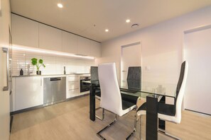 Una cocina moderna con armarios blancos, una mesa de comedor de vidrio y una silla negra.