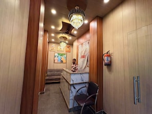 A reception area with a marble counter, a receptionist, and a fire extinguisher on the wall. - Shivala grand guest House Varanasi (Varanasi)