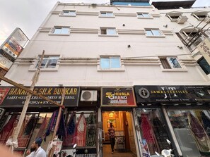 En bygning i flere etager med forskellige butikker i stueetagen, heriblandt en butik med silkevarer og en tekstilforretning.
