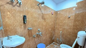 Un baño con lavamanos, inodoro, ducha y un cubo azul en el suelo.
