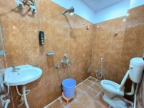 Et badeværelse med vask, toilet og bruser samt en blå balje på gulvet.