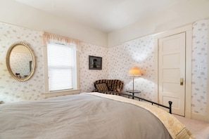 Ein Schlafzimmer mit Bett, Stuhl, Lampe, Tür und Spiegel.