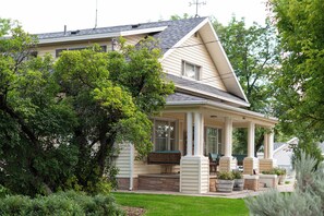 Ett tvåvåningshus med en inglasad veranda, en skorsten och ett stort träd på framsidan av tomten.