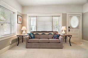 A living room with a beige sofa, two side tables with lamps, a door, and large windows with blinds. - Kanarraville Home - Near Zion & Kanarra Falls (Cedar City)