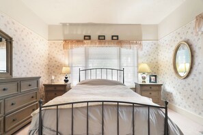 A bedroom with a bed, nightstands, a dresser, a window with blinds, a mirror, and a floral wallpaper pattern. - Kanarraville Home - Near Zion & Kanarra Falls (Cedar City)