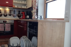 Une cuisine équipée d’un lave-vaisselle, d’une machine à café et d’une fenêtre avec un rideau.