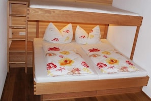 Ein Stockbett mit Holzrahmen, das untere Bett mit einer blumigen Tagesdecke und eine Leiter auf der linken Seite.