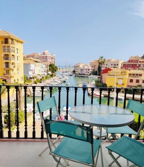 A balcony with a round table and chairs, overlooking a marina with boats and colorful buildings. - Elegant Coastal Apartment with Marina & Beach View (Port Saplaya)