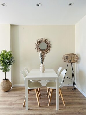 A dining area with a white table, four chairs, a decorative mirror, a potted plant, and a floor lamp. - Elegant Coastal Apartment with Marina & Beach View (Port Saplaya)