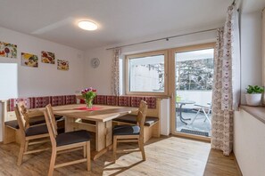 A dining area with a wooden table and chairs, a small plant, and a view through a window. - Holiday apartment with 1 bedroom (Ramsau)