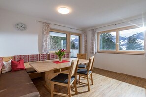 Une pièce comprenant une table à manger en bois, des chaises, un canapé, une horloge et de grandes fenêtres donnant sur la montagne.
