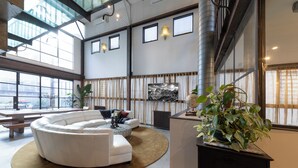 A spacious living area with a white sectional sofa, a round coffee table, and a large potted plant. - Melbourne City Apartments Luxury Loft House with rooftop (Southbank)